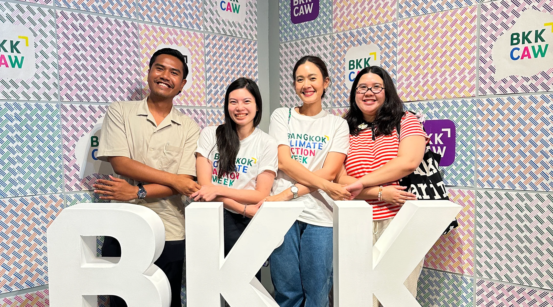 Four Love Frankie team members standing behind large white “BKK” letters at a Bangkok Climate Action Week photo wall